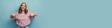 Genç mutlu kadın gülümsüyor ve mavi arka planda kendini işaret ediyor.