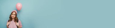 Sırt çantalı genç beyaz kız mavi arka planda izole edilmiş balonla poz veriyor.