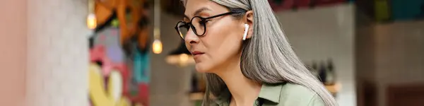 在室内咖啡店与策划者一起工作的戴耳机的成熟的灰色女人 — 图库照片