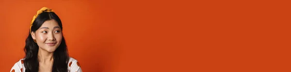 Улыбающаяся Молодая Азиатка Летней Одежде Стоящая Оранжевом Фоне Глядя Сторону — стоковое фото