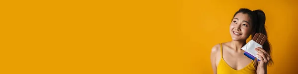 Glückliche Junge Asiatische Brünette Mit Sonnenbrille Und Schokoriegel Vor Gelbem — Stockfoto