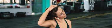 Spor salonunda spor yaparken kulaklıklı beyaz kadın spor paspası üzerinde egzersiz yapıyor.