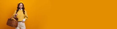 Sarı arka planda izole edilmiş ekmek sepeti taşıyan zarif kızıl saçlı kadın.