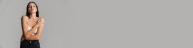 Genç esmer kadın sütyenli poz veriyor ve gri arka planda izole edilmiş kameraya bakıyor.