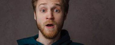 Sakallı beyaz kızıl adam gri arka planda izole edilmiş kameraya şaşırdığını ifade ediyor.