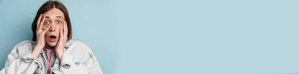 Молодий Шокований Чоловік Прикриває Обличчя Висловлюючи Несподіванку Ізольовано Синьому Фоні — стокове фото