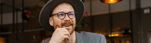 一个戴着眼镜 头戴帽子 头戴笔记本电脑的中年时尚嬉皮士坐在咖啡桌旁微笑着 手里拿着杯子 — 图库照片