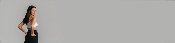 Молодая белая женщина с длинными волосами брюнетки в кукурузном топе, стоящая на сером фоне