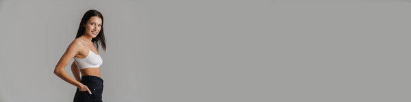 Улыбающаяся молодая белая женщина с длинными волосами брюнетки в кукурузном топе, стоящая на сером фоне