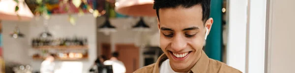 Usmívající Mladý Hispánec Sluchátkách Videohovoru Přes Mobilní Telefon Stojící Kavárně — Stock fotografie