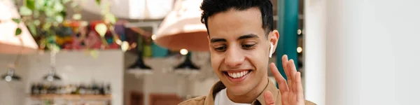Улыбающийся Молодой Латиноамериканец Наушниках Видеозвонке Через Мобильный Телефон Стоящий Кафе — стоковое фото