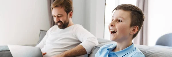 快乐的父亲和小儿子在家里玩电子游戏 父亲在笔记本电脑上工作 — 图库照片