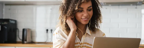 stock image A happy black woman in a wired headphones sitting in front of laptop in the white kitchen