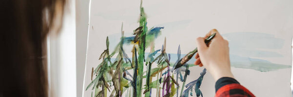 Молодая белая художница держит кисть, стоящую на холсте в закрытом помещении.