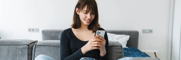 Smilende Ung Kvinne Som Bruker Mobiltelefon Mens Hun Sitter Sofaen – stockfoto