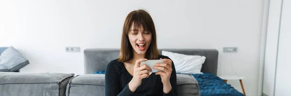 Smilende Ung Kvinne Som Bruker Mobiltelefon Mens Hun Sitter Sofaen – stockfoto