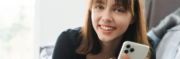 Hymyilevä Nuori Nainen Tilalla Matkapuhelin Tekstiviesti Kun Makaa Sohvalla Kotona — kuvapankkivalokuva