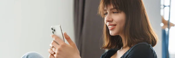 Smilende Ung Kvinne Som Holder Mobiltelefon Mens Hun Lener Seg – stockfoto
