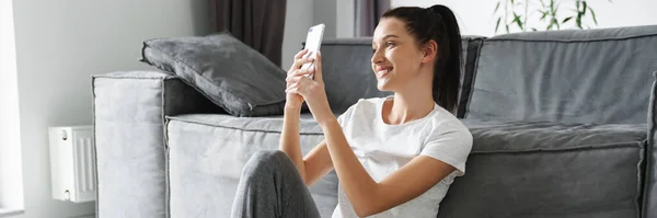 Europejska Uśmiechnięta Kobieta Korzystająca Telefonu Komórkowego Podczas Siedzenia Podłodze Domu — Zdjęcie stockowe