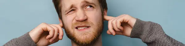 Bearded Ginger Man Frowning While Plugging His Ears Isolated Blue — Stock Photo, Image