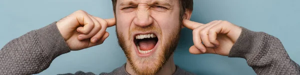 Бородатый Рыжий Человек Кричит Закрывая Уши Изолированным Синем Фоне — стоковое фото
