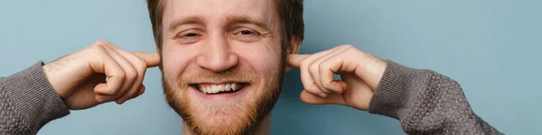 Vousatý Zrzavý Muž Usmívá Zacpává Uši Modrém Pozadí — Stock fotografie