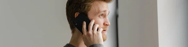 Roodharige Jongeman Praten Mobiele Telefoon Terwijl Staande Binnen — Stockfoto