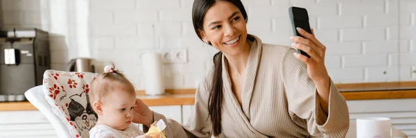 Joven Madre Tomando Selfie Teléfono Móvil Con Bebé Cocina Casa —  Fotos de Stock