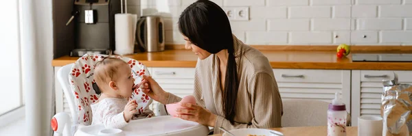 Young Brunette Mother Smiling Feeding Her Baby Kitchen Home — Stock Photo, Image