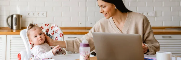 Young Mother Working Laptop While Keeping Her Baby Kitchen Home — Stock Photo, Image