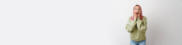 Молодая возбужденная женщина с розовыми волосами выражает удивление перед камерой на белом фоне