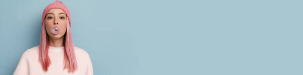 Молодая женщина в розовой шляпе выдувая жвачку на голубом фоне