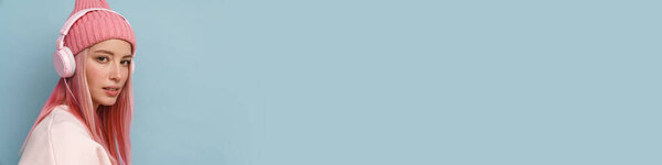 Молодая белая женщина в розовой шляпе слушает музыку с наушниками изолированы над синей стеной