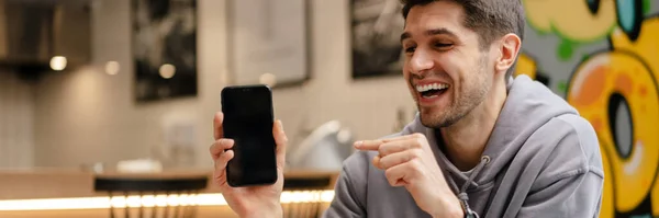Šťastný Mladý Bruneta Muž Ukazující Prázdné Obrazovky Mobilní Telefon Zatímco — Stock fotografie