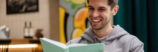Glimlachende Jongeman Boek Lezen Tijdens Het Studeren Cafe Binnen — Stockfoto