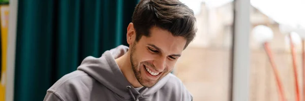 Hymyilevä Nuori Mies Lukee Kirjaa Opiskellessaan Kahvilassa Sisätiloissa — kuvapankkivalokuva