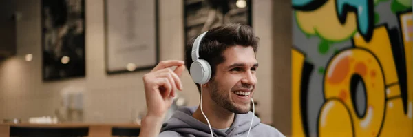 Χαμογελώντας Νεαρός Casual Άνθρωπος Ακουστικά Ακούγοντας Μουσική Κρατώντας Κινητό Τηλέφωνο — Φωτογραφία Αρχείου