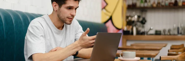 Hämmentynyt Nuori Mies Opiskelija Istuu Kahvilassa Sisällä Kannettavan Tietokoneen Kanssa — kuvapankkivalokuva