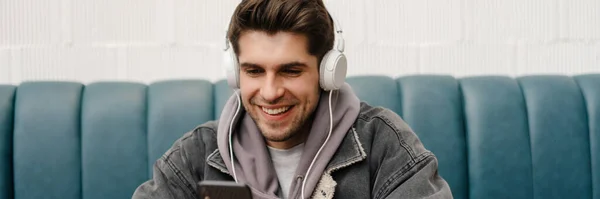 Hymyilevä Nuori Rento Mies Kuulokkeissa Kuuntelemassa Musiikkia Pitämässä Matkapuhelinta Istuessaan — kuvapankkivalokuva
