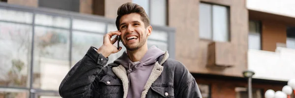 stock image Smiling young white man in casual cothes using mobile phone outdoors in the city, walking