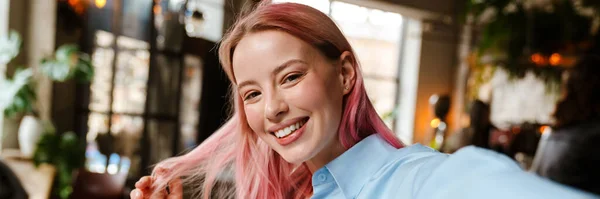 カフェで勉強しながらピンク色の髪の若い美しい女性が自撮り写真を撮る — ストック写真