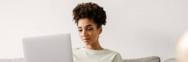 Young black woman working with laptop while sitting on couch at home