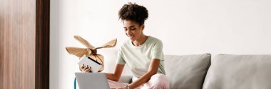 Young black woman using tablet computer while working with laptop at home
