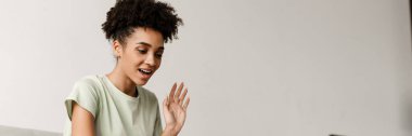 Young black woman gesturing and using laptop while sitting on couch at home