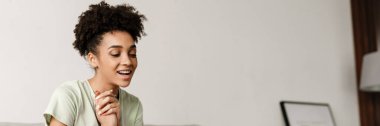 Young black woman gesturing and using laptop while sitting on couch at home