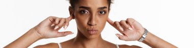 Young black woman in tank top making kiss lips and plugging her ears isolated over white background