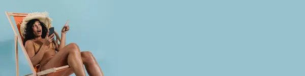 Черная Шокированная Женщина Помощью Мобильного Телефона Сидя Шезлонге Изолированы Синем — стоковое фото
