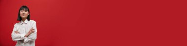 Genç Asyalı esmer kadın kırmızı arka planda yalnız poz veriyor ve kameraya bakıyor.