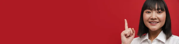 Молодая Азиатская Женщина Рубашке Улыбается Указывает Пальцем Вверх Красный Фон — стоковое фото