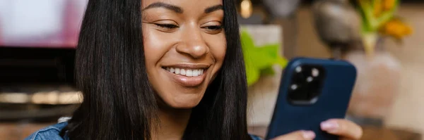 Hymyilevä Nuori Afrikkalainen Nainen Käyttää Matkapuhelinta Istuessaan Kahvilassa — kuvapankkivalokuva